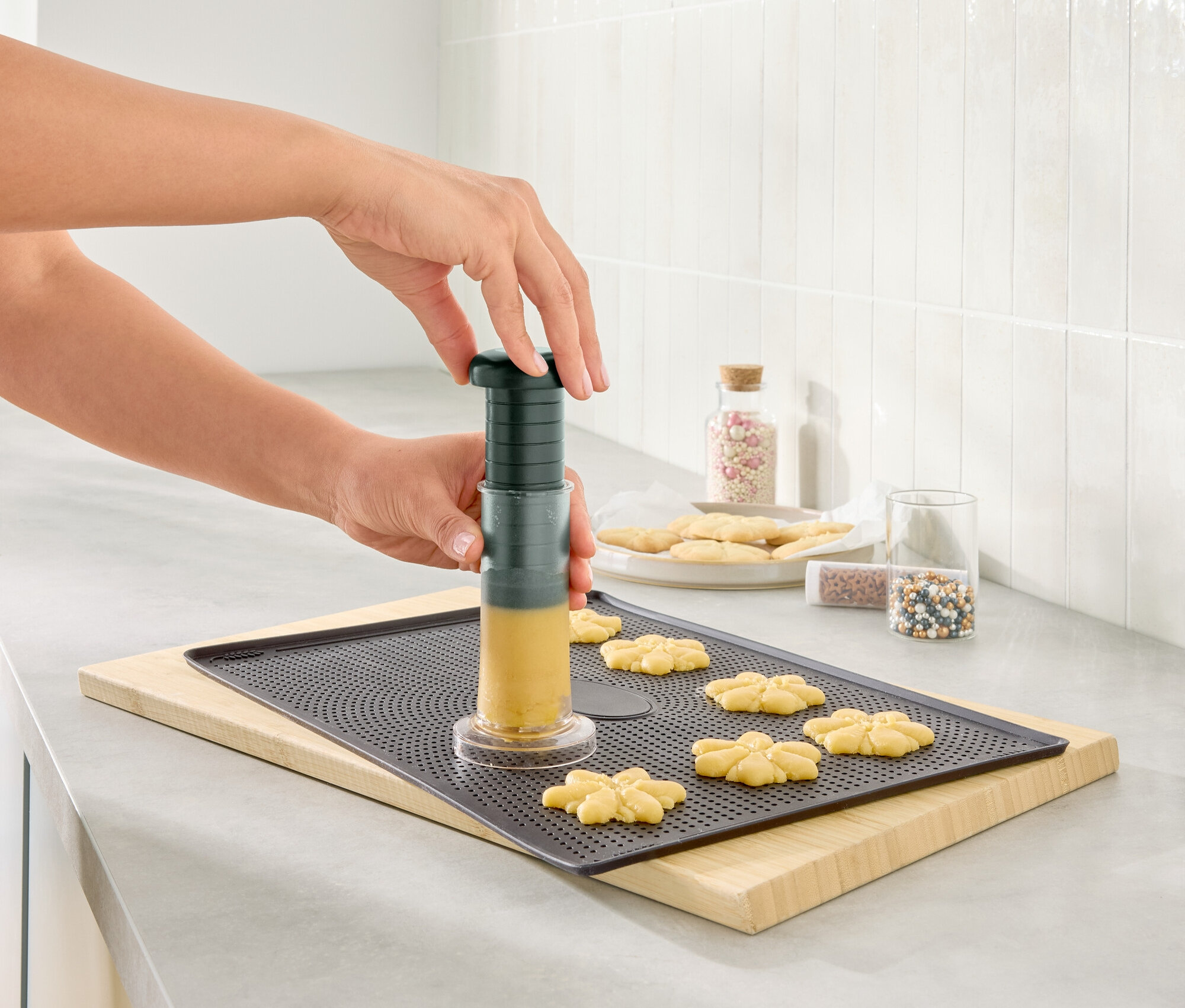 Frau formt Teig mit einer Kekspresse auf einem Backblech.