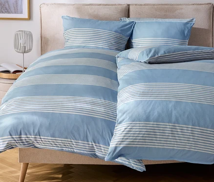 Bett mit blau-weiß gestreifter Bettwäsche und Kissen.