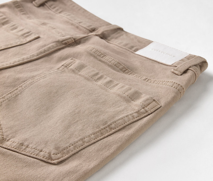 Detailaufnahme einer beigen Jeans mit Taschen und Logo-Patch.