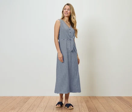 Frau steht in einem blau-weiß gestreiften Kleid und blauen Sandalen.