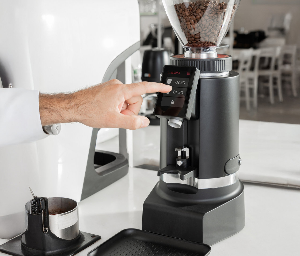 Eine Person tippt auf den Bildschirm einer schwarzen Kaffeemühle, die auf einer weißen Theke steht.