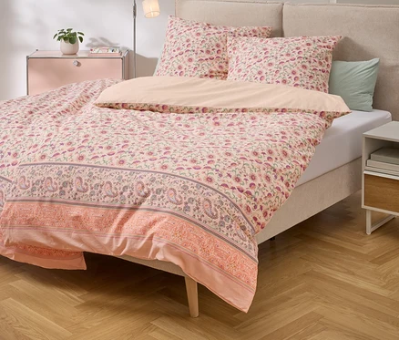 Bett mit rosa Blumenmuster-Bettwäsche und passenden Kissen auf einem Holzboden.