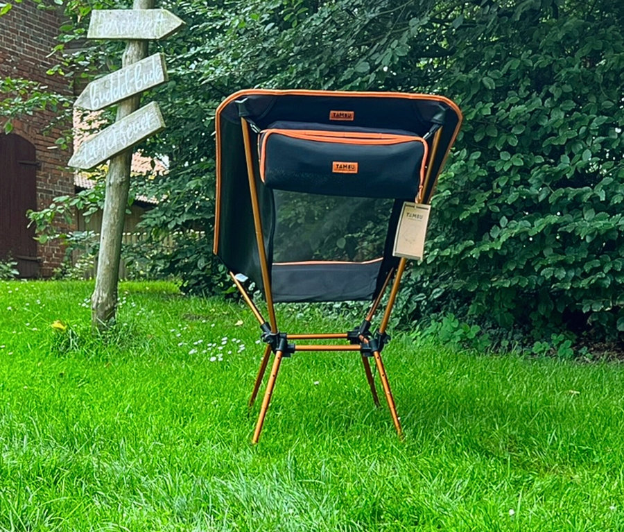 Der Tambu Campingstuhl »BATASA COMFORT« steht auf einer Wiese neben einem Wegweiser.