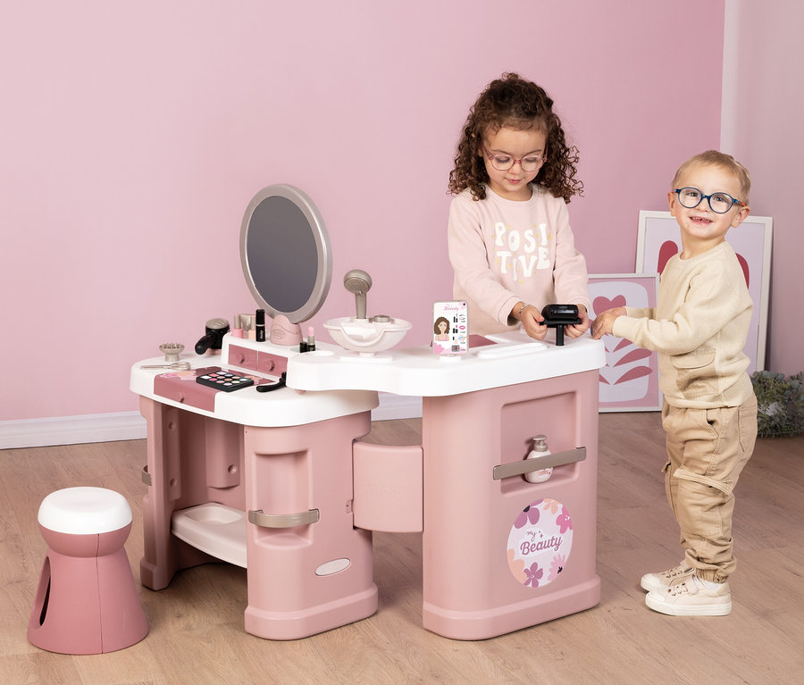 Zwei Kinder spielen mit dem Smoby My Beauty Center Kosmetikstudio, das mit Spielzeug-Kosmetikartikeln ausgestattet ist.