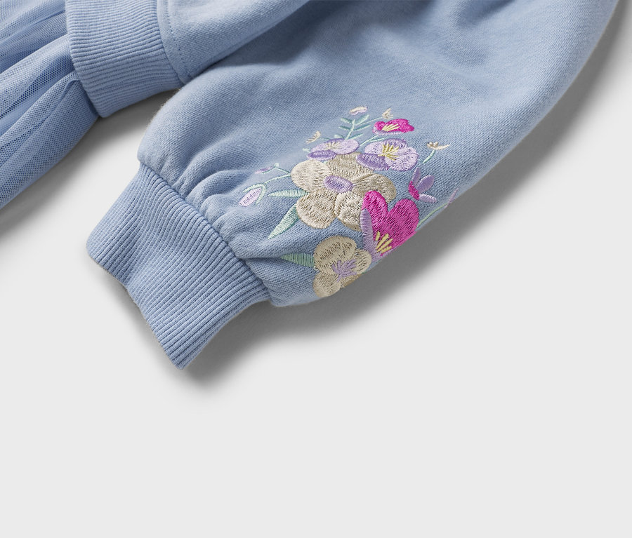 Nahaufnahme eines hellblauen Sweatshirts mit Blumenstickerei am Ärmel und einem gerippten Bündchen.