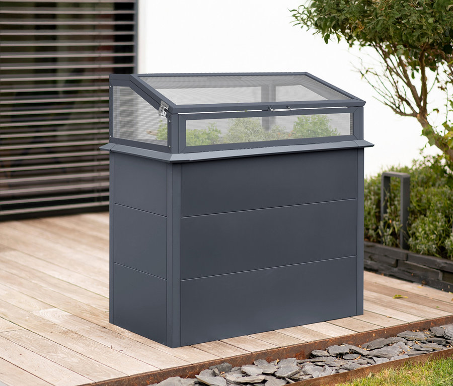 Draußen steht ein anthrazitfarbenes Hochbeet mit Schneckenschutz und Frühbeetaufsatz, sowie ein Metall-Hochbeet mit Stauraum und Aufsatz auf einer Terrasse.