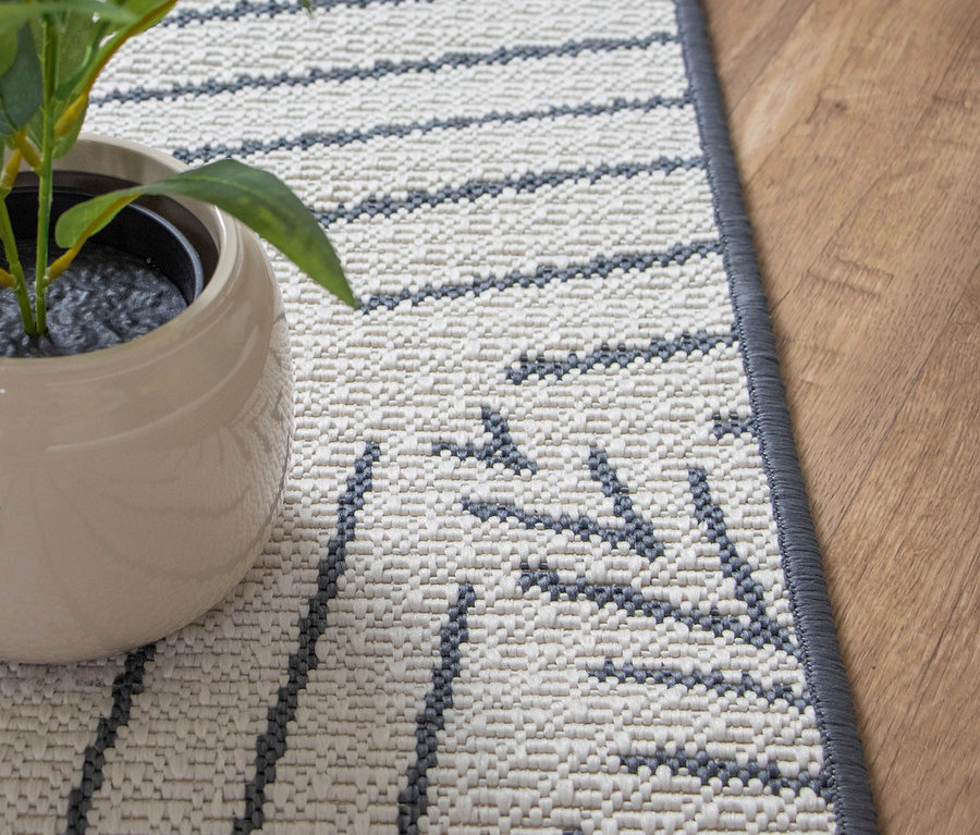 Nahaufnahme eines Teppichs mit grauem Muster und einer Topfpflanze.