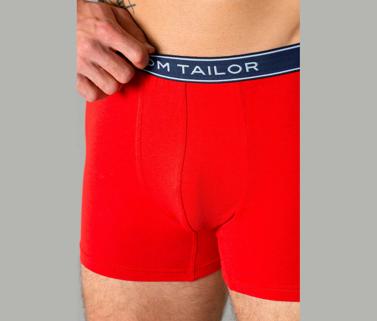 Mann trägt rote Boxershorts mit einem marineblauen Bund mit dem Text 'TOM TAILOR'.