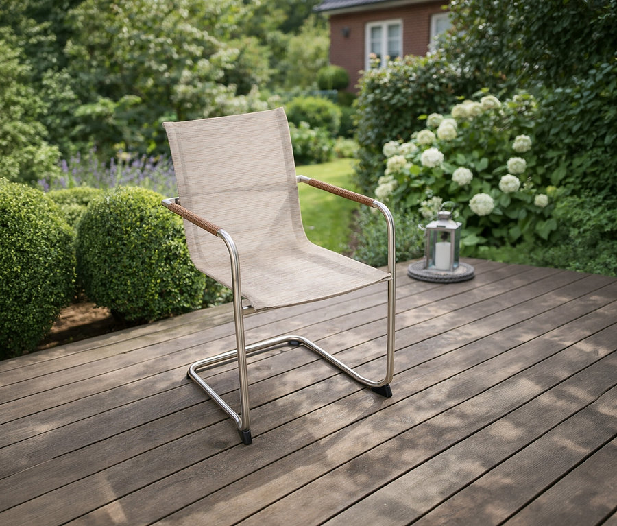 Ein einzelner »Nova« Freischwinger mit silbernem Gestell und beigem Stoffbezug steht auf einer Holzterrasse im Garten.