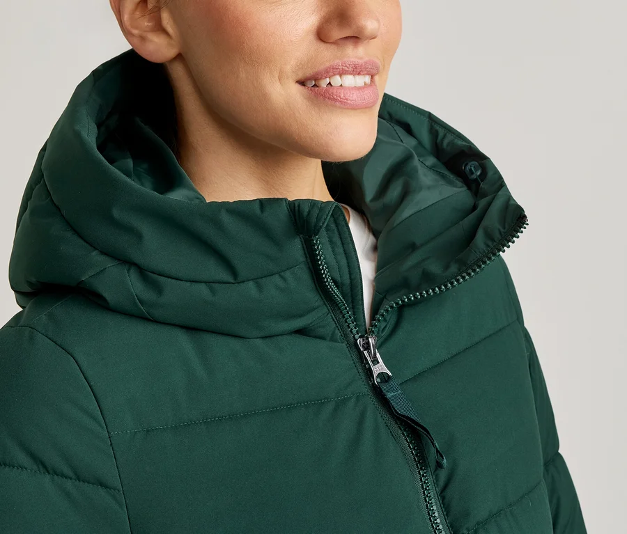 Frau mit grünem Puffer-Hoodie, Reißverschluss halb geschlossen.