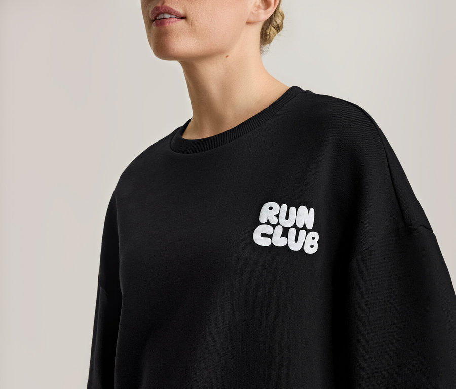 Frau trägt ein schwarzes Sweatshirt mit weißem "RUN CLUB"-Aufdruck.