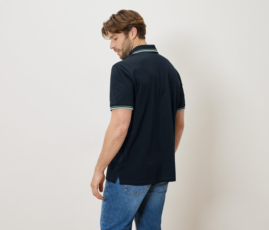 Mann von hinten in marineblauem Poloshirt mit Jeans. Kragen und Ärmel haben grüne Streifen.