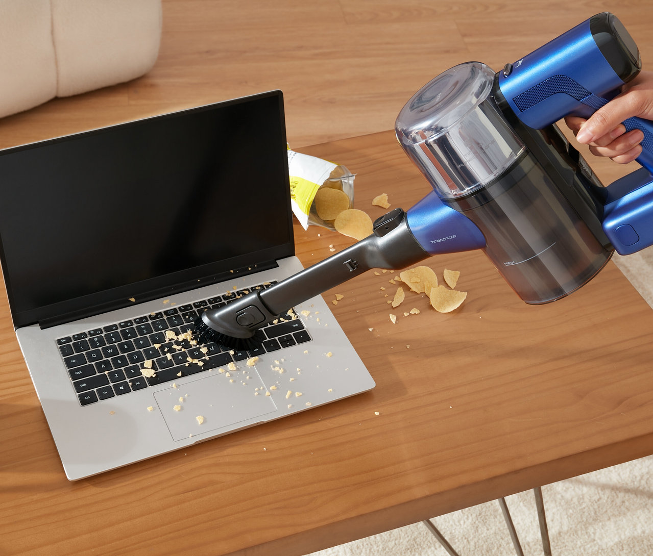 Person saugt Krümel mit einem blauen Tineco Akku-Staubsauger »Pure One S50 Pro« von einer Laptop-Tastatur.