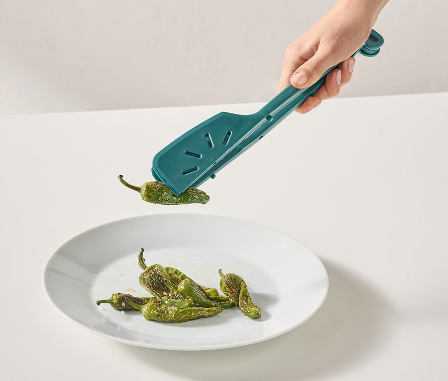Eine Hand platziert mit einer türkisfarbenen Zange grüne Paprika auf einen Teller.