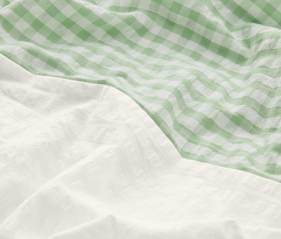 Nahaufnahme von zerknitterter Bettwäsche: ein Teil ist weiß, der andere grün-weiß kariert.