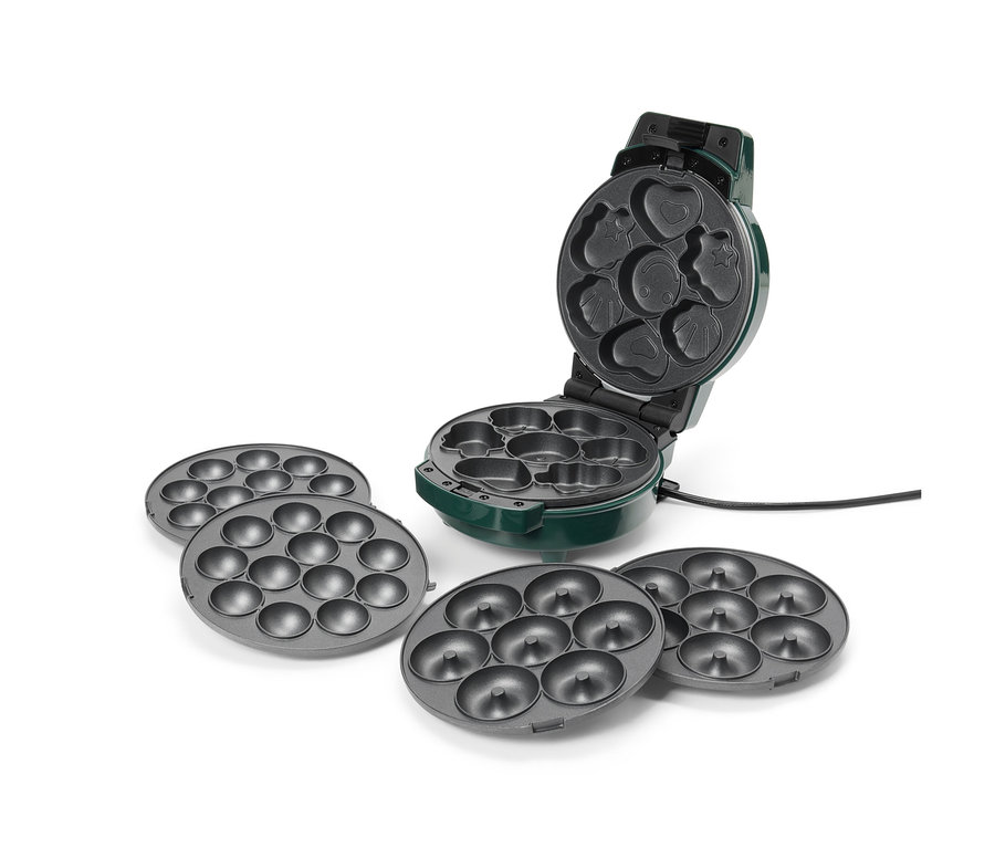 Ein grüner Donut-Maker ist geöffnet und hat verschiedene Formen, darunter ein Herz, ein Stern und ein Smiley. Zum Maker gehören vier graue Donutbleche.
