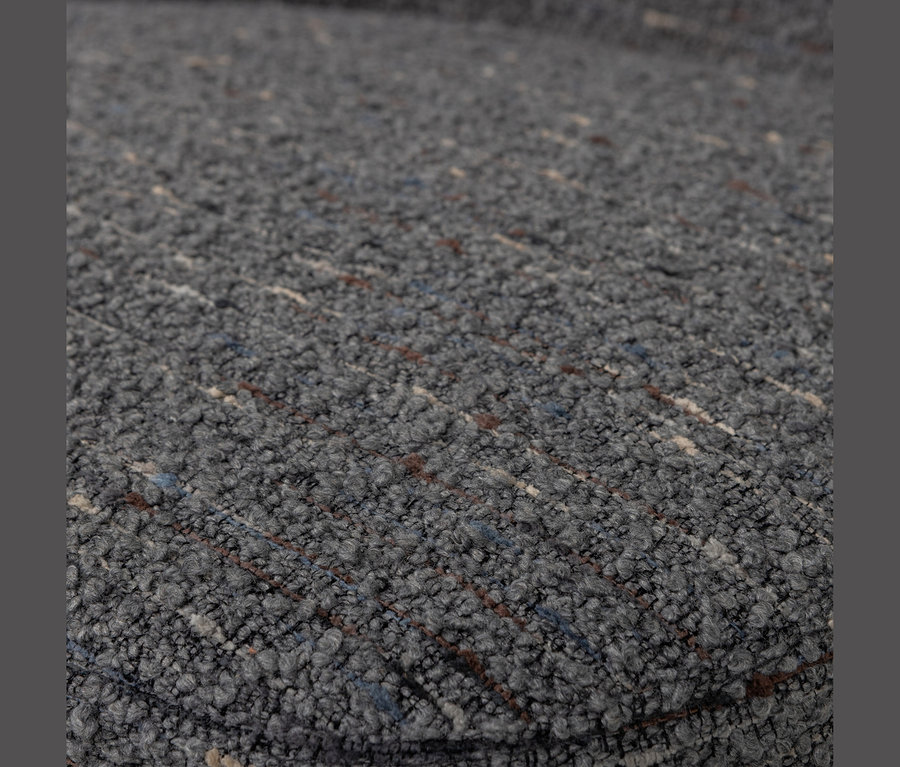 Nahaufnahme eines dunkelgrauen, strukturierten Stoffes mit subtilen blauen, braunen und weißen Sprenkeln. Der Stoff hat eine Schlingen- oder Bouclé-Textur, die eine raue Oberfläche erzeugt.