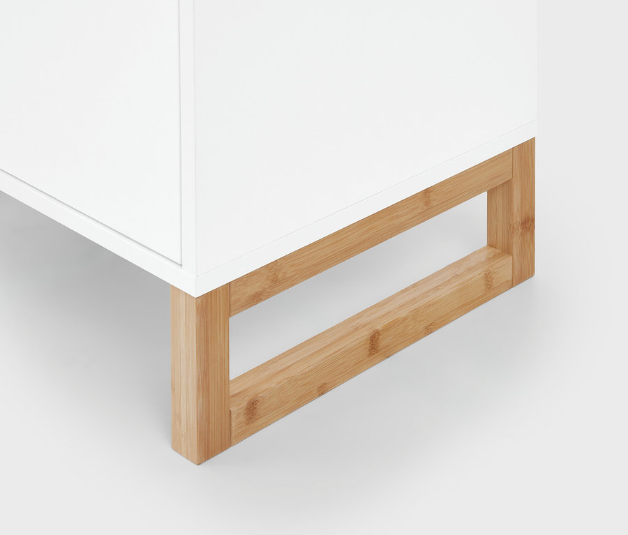 Untere Ecke eines weißen Möbelstücks mit hellem, bambusartigem Holzsockel.