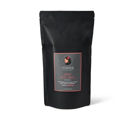 Schwarze Packung Yoanda Küsst Dich Wach Espresso, 1 kg ganze Bohne. Auf dem Etikett ist eine stilisierte Frau mit Blume abgebildet.