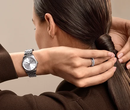 Frau bindet ihre Haare zu einem Pferdeschwanz zusammen, trägt eine silberne Uhr und einen Ring.