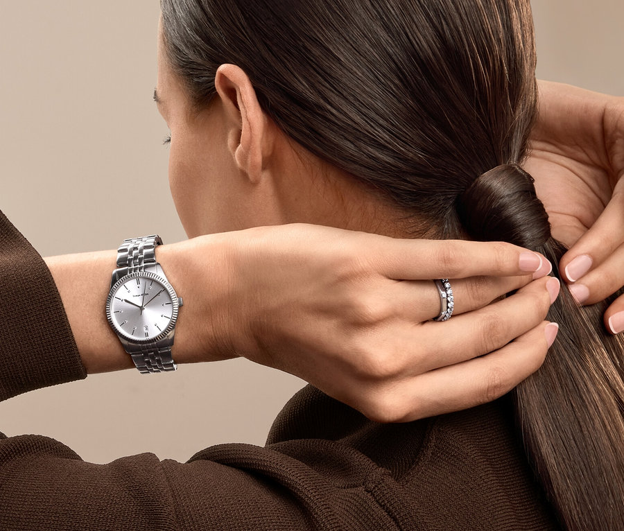 Frau bindet ihre Haare zu einem Pferdeschwanz zusammen, trägt eine silberne Uhr und einen Ring.