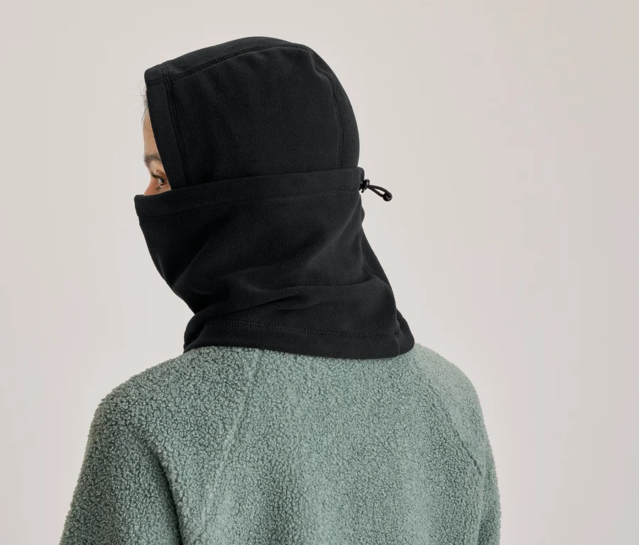 Person von hinten, trägt eine schwarze Sturmhaube, die Kopf und Hals bedeckt, mit Kordelzug und einer grünen Fleecejacke.