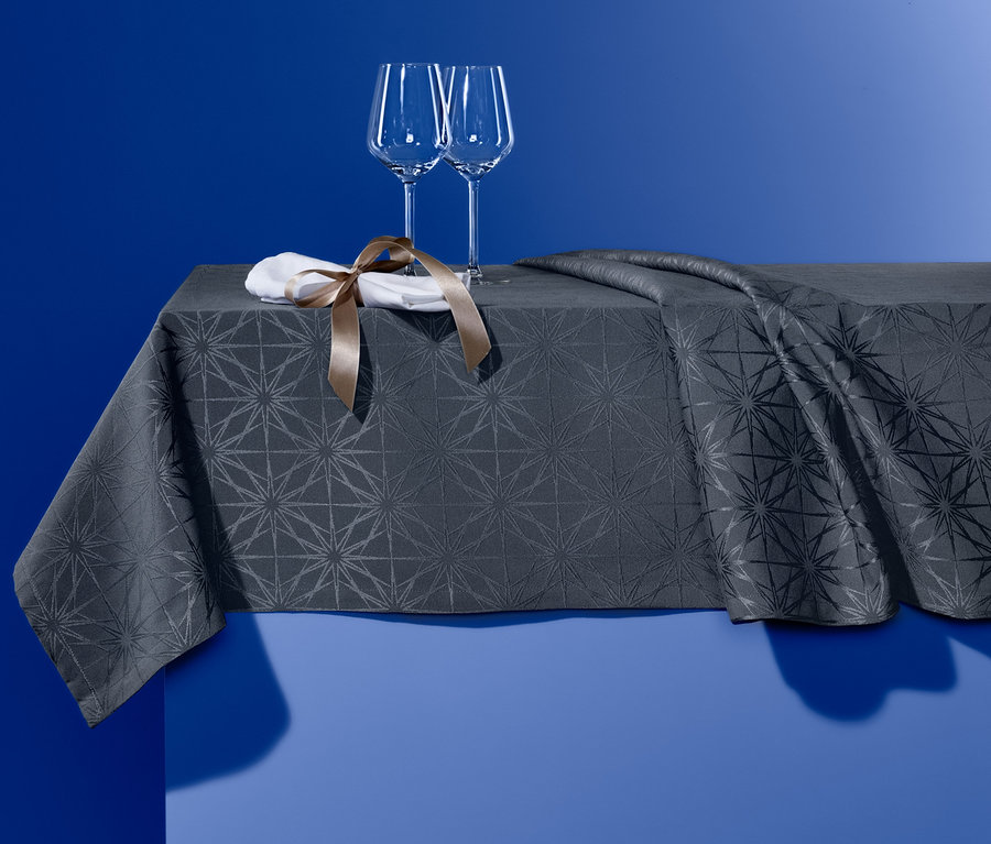 Zwei Weingläser und eine Serviette mit braunem Band stehen auf einer Jacquard-Tischdecke.
