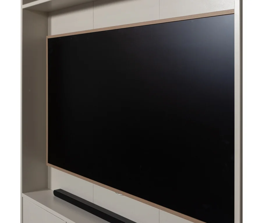 Großer schwarzer Bildschirm mit dünnem Holzrahmen, montiert auf einer hellen Wandeinheit, darunter eine schwarze Soundbar.