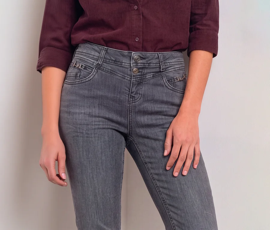 Person trägt ein weinrotes Langarmshirt und eine graue Street One Jeans mit hohem Bund, zwei Knöpfen und dekorativen Reißverschlüssen an den Vordertaschen.