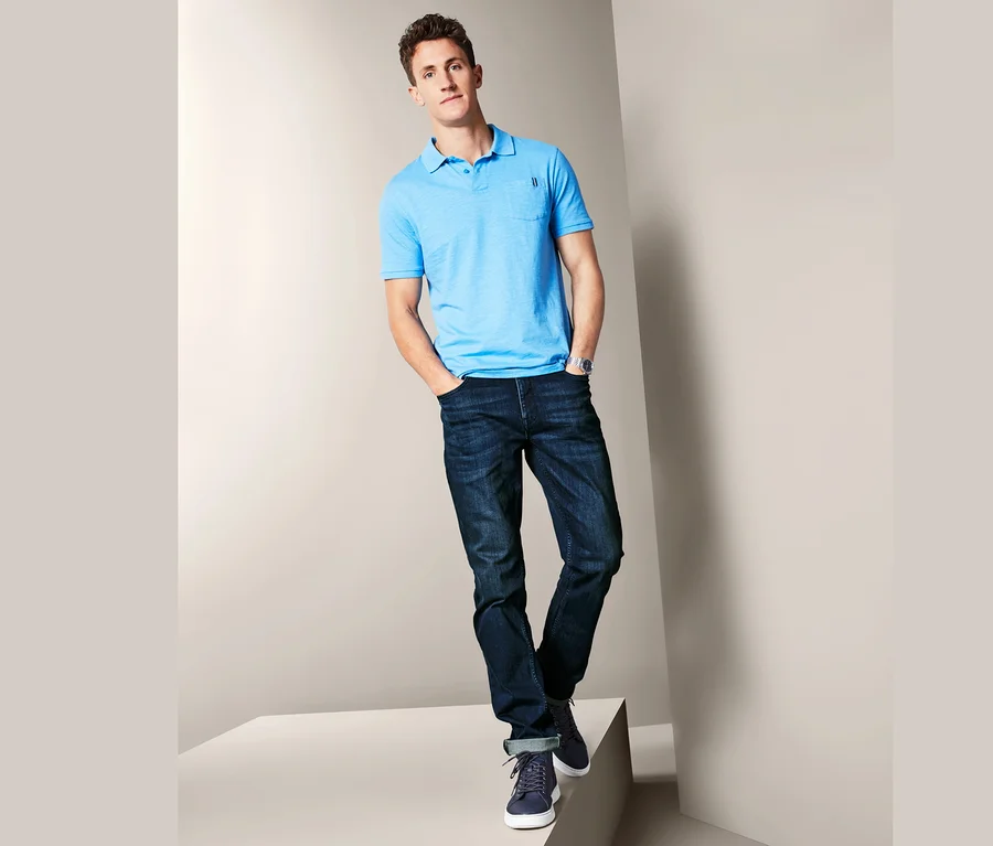 Mann posiert auf einem Podest und trägt Jeans und ein blaues Poloshirt.