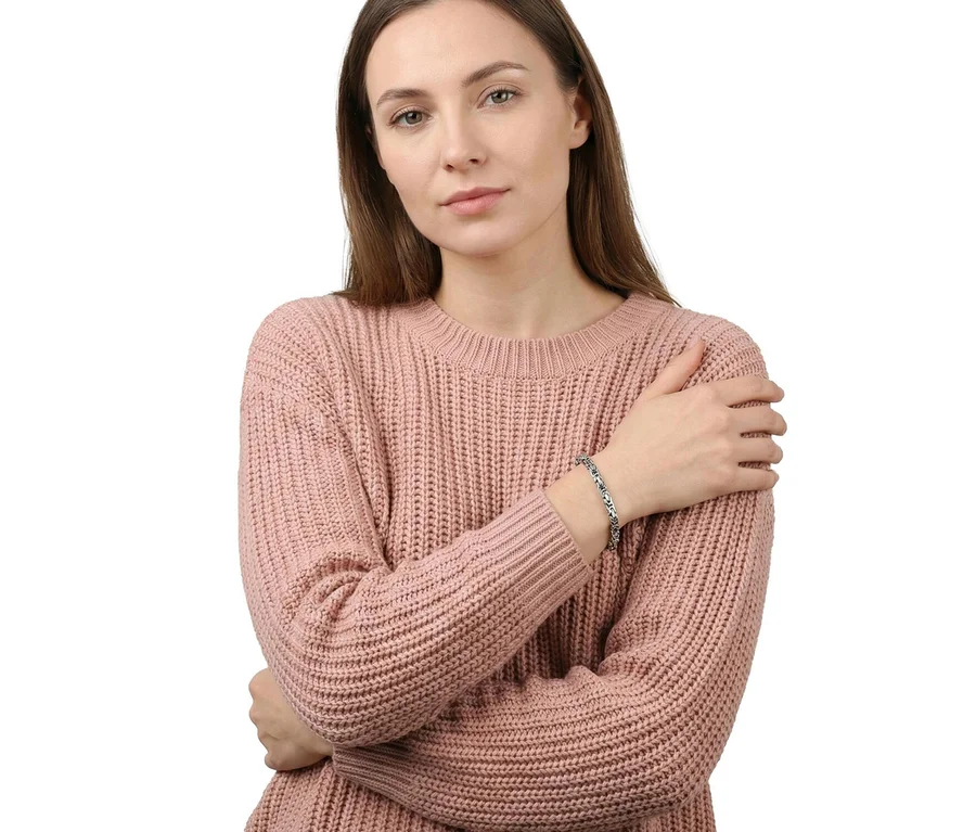 Frau in rosa Strickpullover trägt einen Amor Glieder-Armschmuck am rechten Handgelenk, die Arme verschränkt.