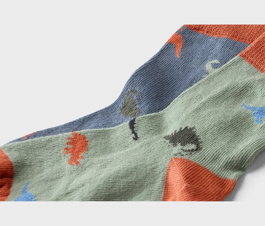 Nahaufnahme von zwei Socken mit Dinosaurier-Motiv in Grün- und Blautönen mit orangefarbenen Zehen und Fersen.