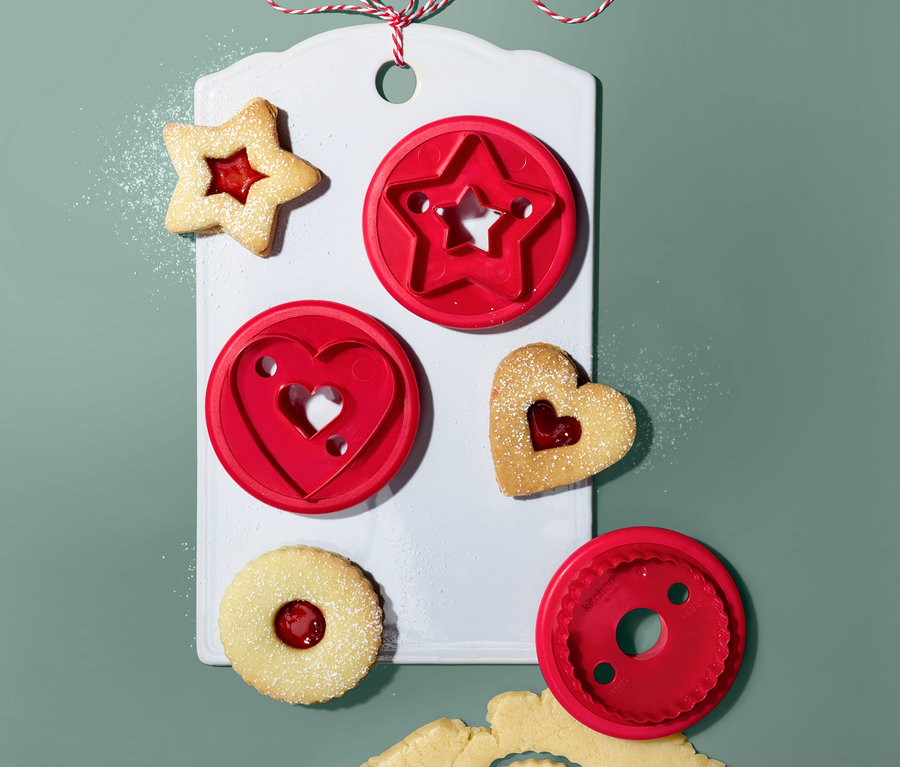 Linzer-Plätzchen-Ausstecher (3 Stk.) auf einem weißen Brett mit Stern-, Herz- und Kreisform. Ausgestochene Formen mit Marmelade und Teig.
