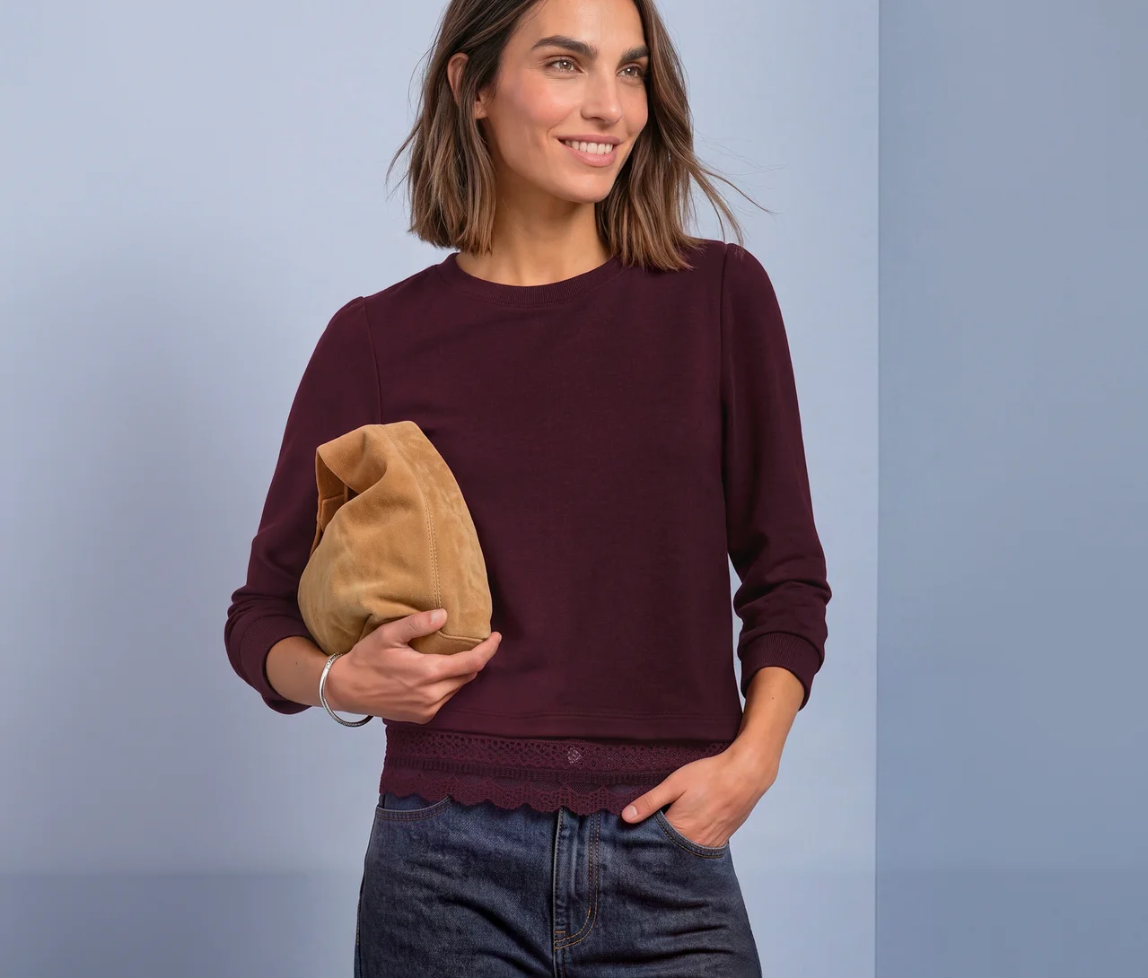 Eine lächelnde Frau mit kurzen braunen Haaren trägt ein rotes Street One 3/4-Jerseyshirt mit Spitzenbesatz, dunkle Jeans und hält eine hellbraune Clutch-Tasche.