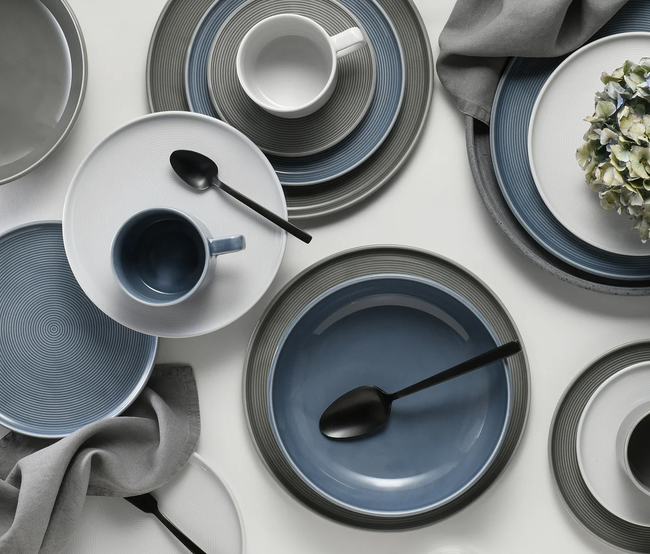 creaTable Service »Session Urban«, 30-teilig, mit Tellern, Schalen und Tassen in Blau, Grau und Weiß, teils mit Ringmuster, auf weißem Untergrund mit schwarzen Löffeln und grauen Servietten.