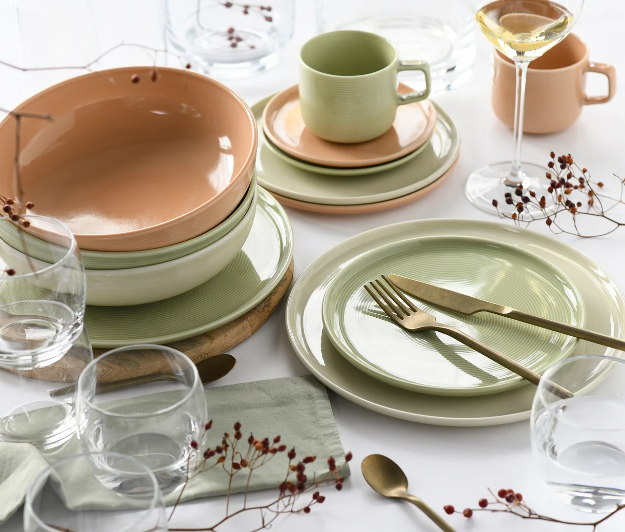 Ein gedeckter Tisch mit dem 30-teiligen creaTable Service "Session Romance" in Hellgrün und Pfirsichfarben, bestehend aus Tellern, Schalen und Tassen, ergänzt durch goldfarbenes Besteck, Gläser und dekorative Beeren-Zweige.