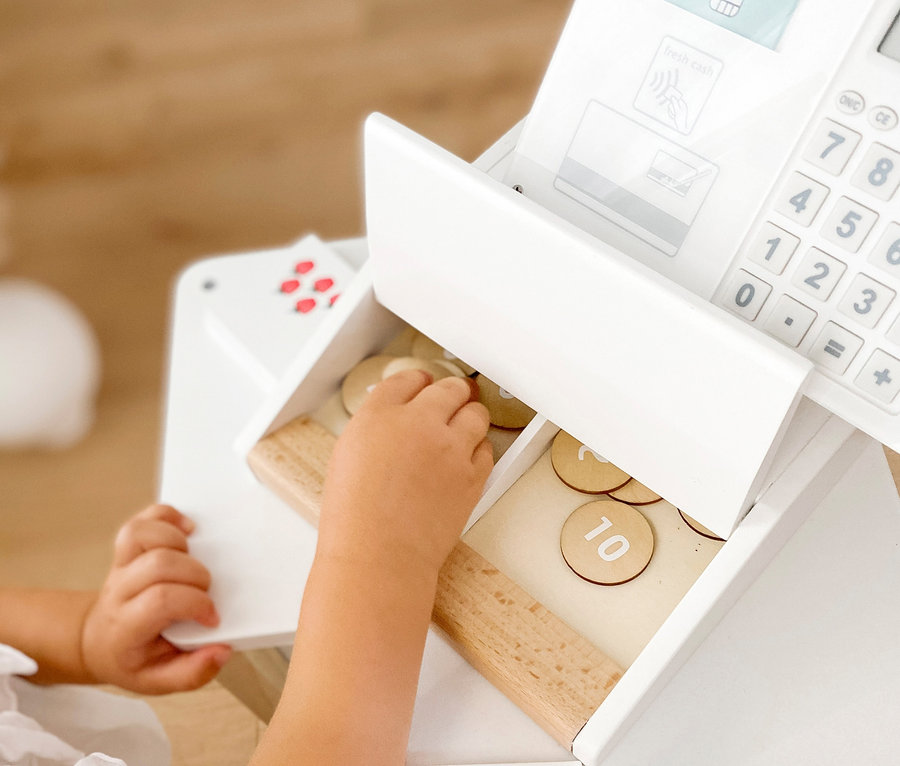 Eine Kinderhand greift in die Schublade einer weißen small foot Kasse »fresh« mit Holzmünzen.