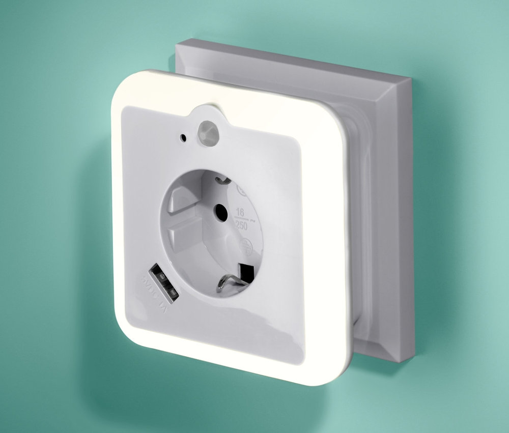 An einer grünen Wand ist ein USB-Netzadapter mit Nachtlicht und Steckdose angebracht.