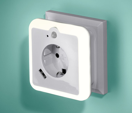 An einer grünen Wand ist ein USB-Netzadapter mit Nachtlicht und Steckdose angebracht.