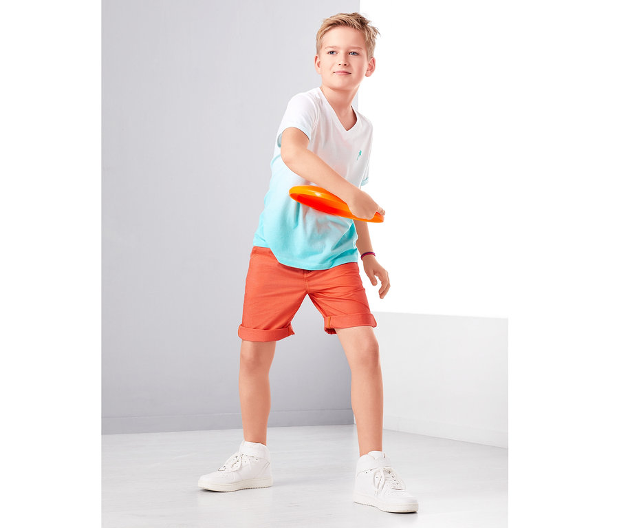 Junge wirft orangefarbene Scheibe. Er trägt Shorts.