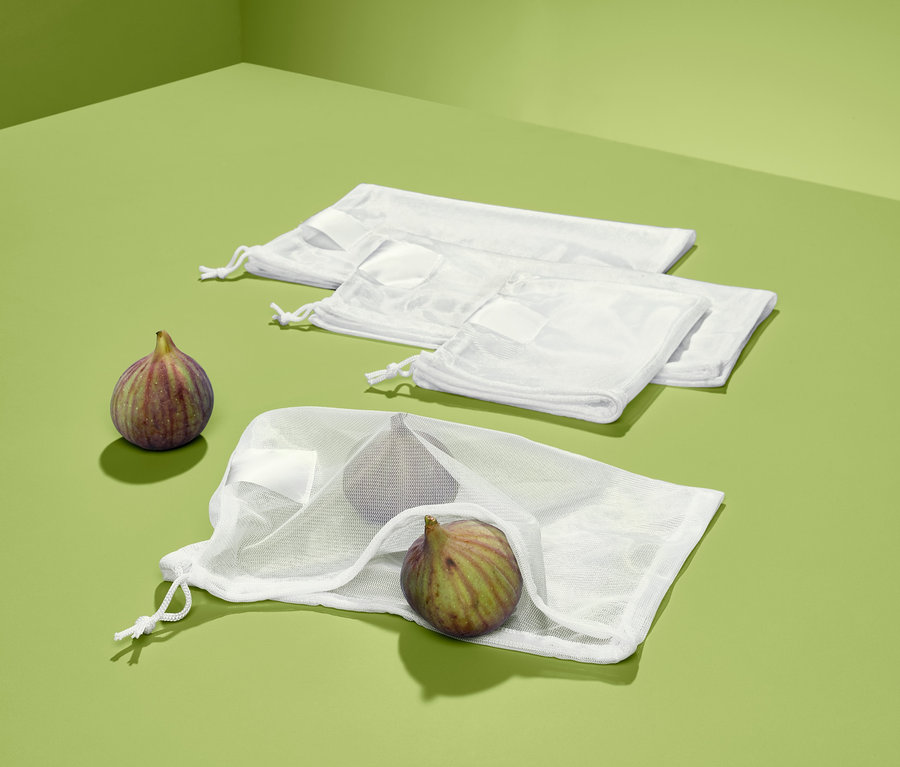 Vier weiße Obst- und Gemüsenetze, eines mit Feigen, liegen auf grünem Hintergrund.