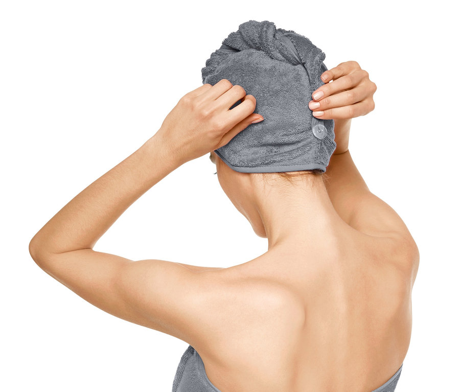 Frau befestigt ein Turban-Handtuch auf ihrem Kopf, während sie in ein Handtuch gewickelt ist.