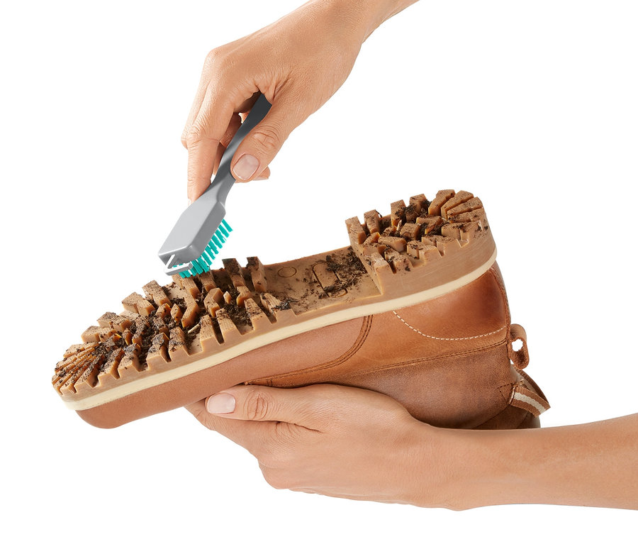 Eine Hand reinigt mit einem Grobschmutz-Schuhsohlenreiniger die Sohle eines braunen Lederschuhs.