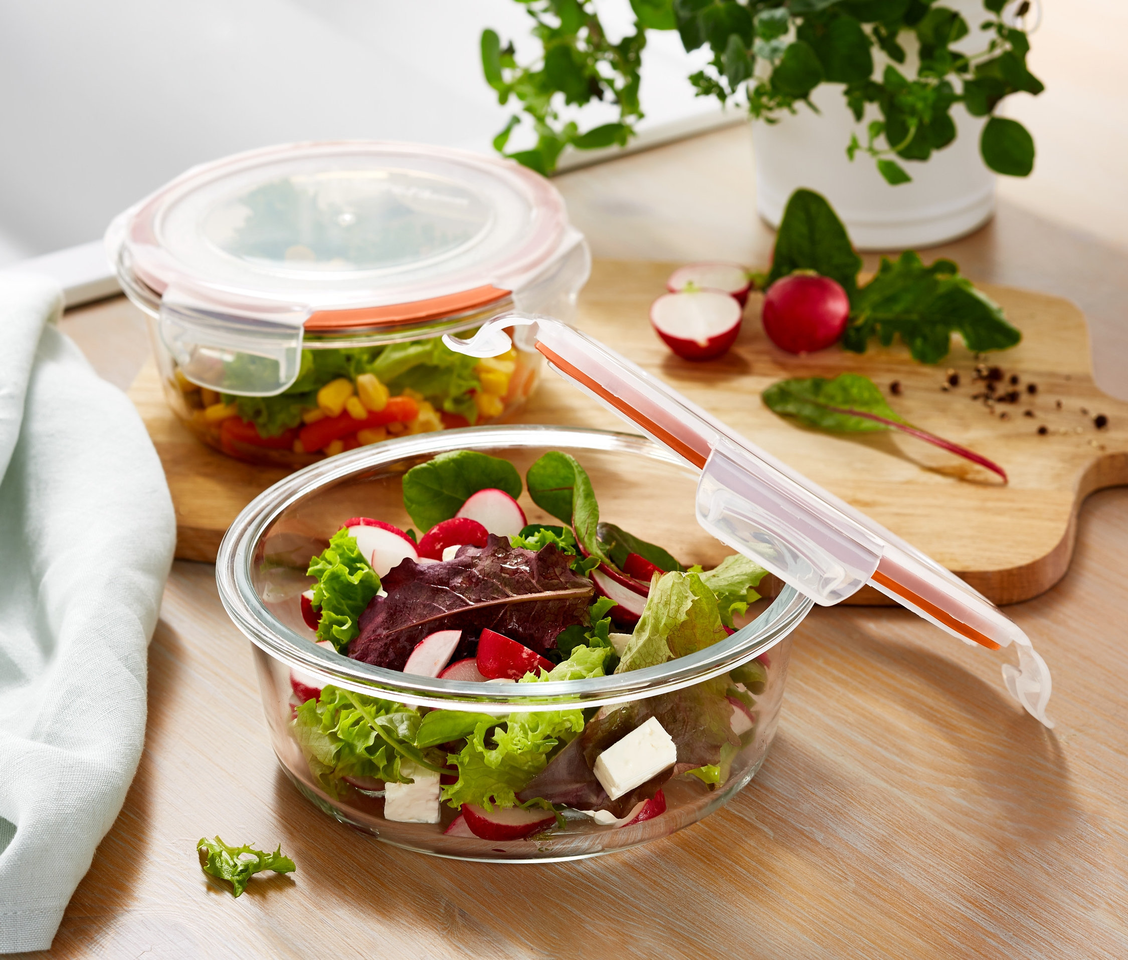 Zwei mit Salat gefüllte Glasschüsseln mit Deckel stehen auf einem Holztisch.