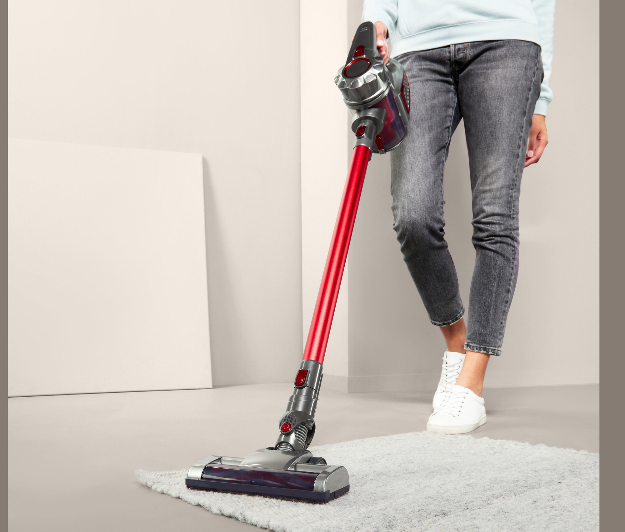 Frau saugt flauschigen Teppich mit Akkusauger.