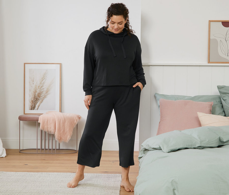 Frau steht barfuß im Schlafzimmer und trägt einen Hausanzug.