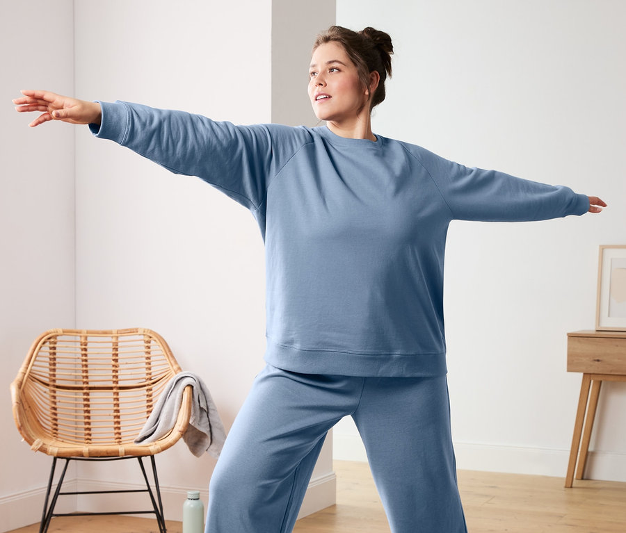 Frau macht Yoga auf einer Matte, trägt ein blaues Yogasweatshirt und eine weite Sweathose. Sie trägt blaue Socken (3 Paar).