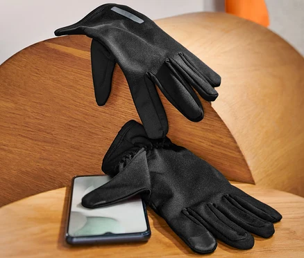 Zwei schwarze Laufhandschuhe liegen auf einem Holztisch neben einem Handy.