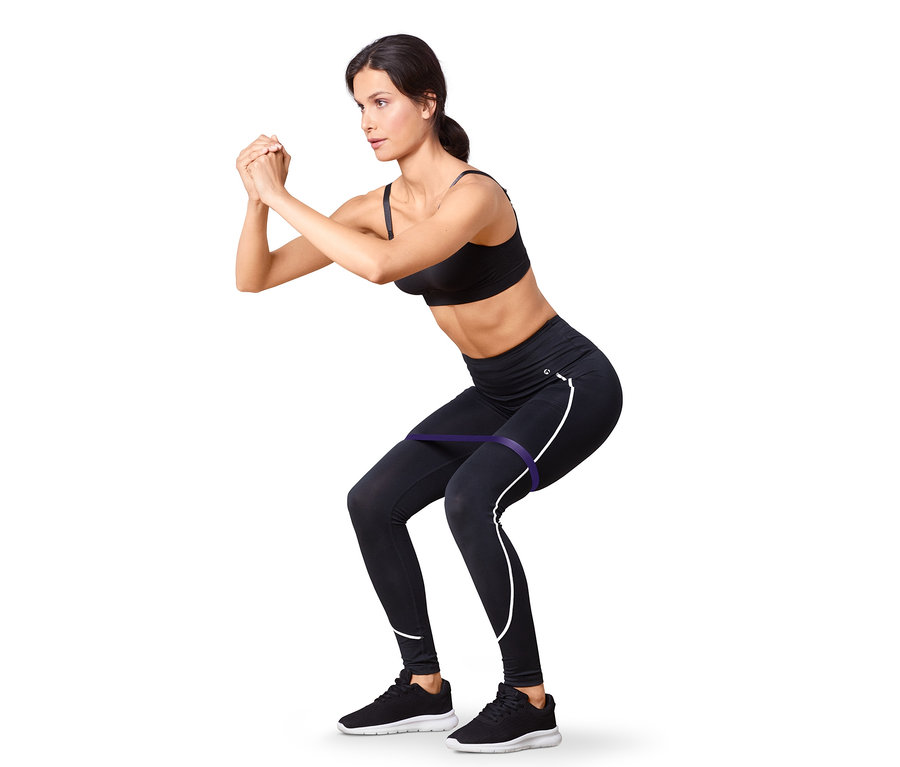 Frau in schwarzem Sport-BH und Leggings macht Kniebeugen mit einem violetten Fitnessband. 2 Fitness- und 2 Mini-Bänder.