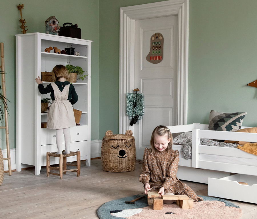 Mädchen steht auf Hocker an weißem Hoppekids Schrank »Hans«, anderes Mädchen spielt am Boden mit Holzspielzeug.